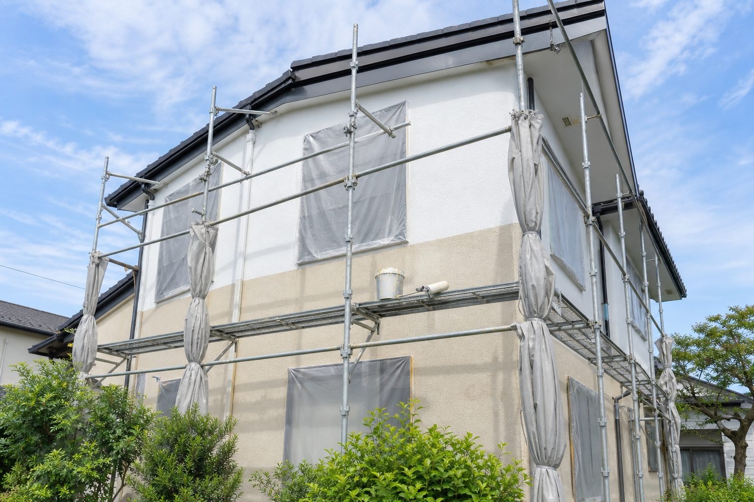 足場が組まれ、上半分が塗り替えられた住宅の外壁